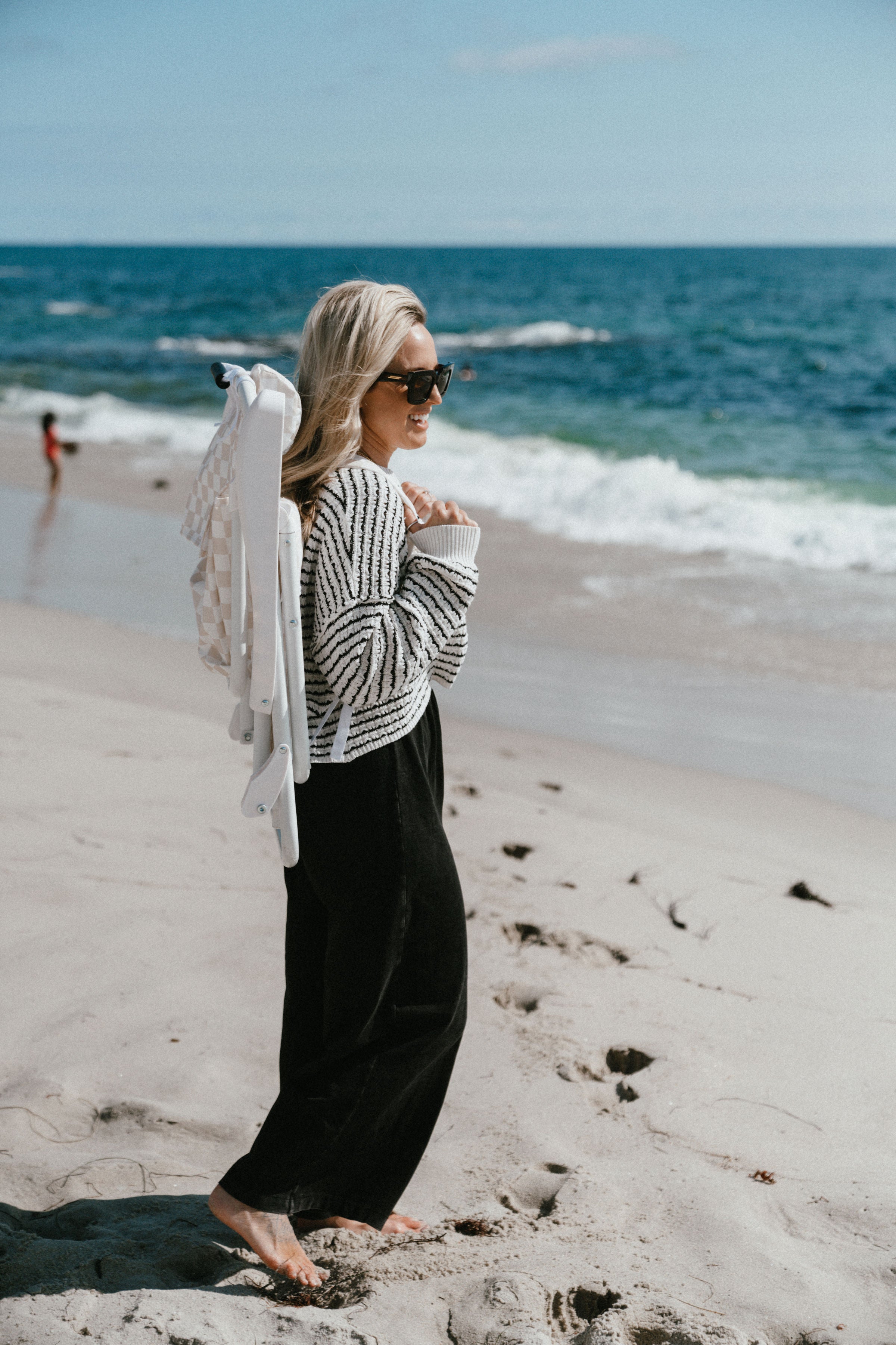 Stylish striped bag with visor cap, sunglasses and blanket on sandy beach  near sea Stock Photo